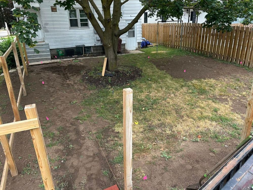 Backyard renovation with marked areas, wooden posts, and a tree, ready for landscaping.