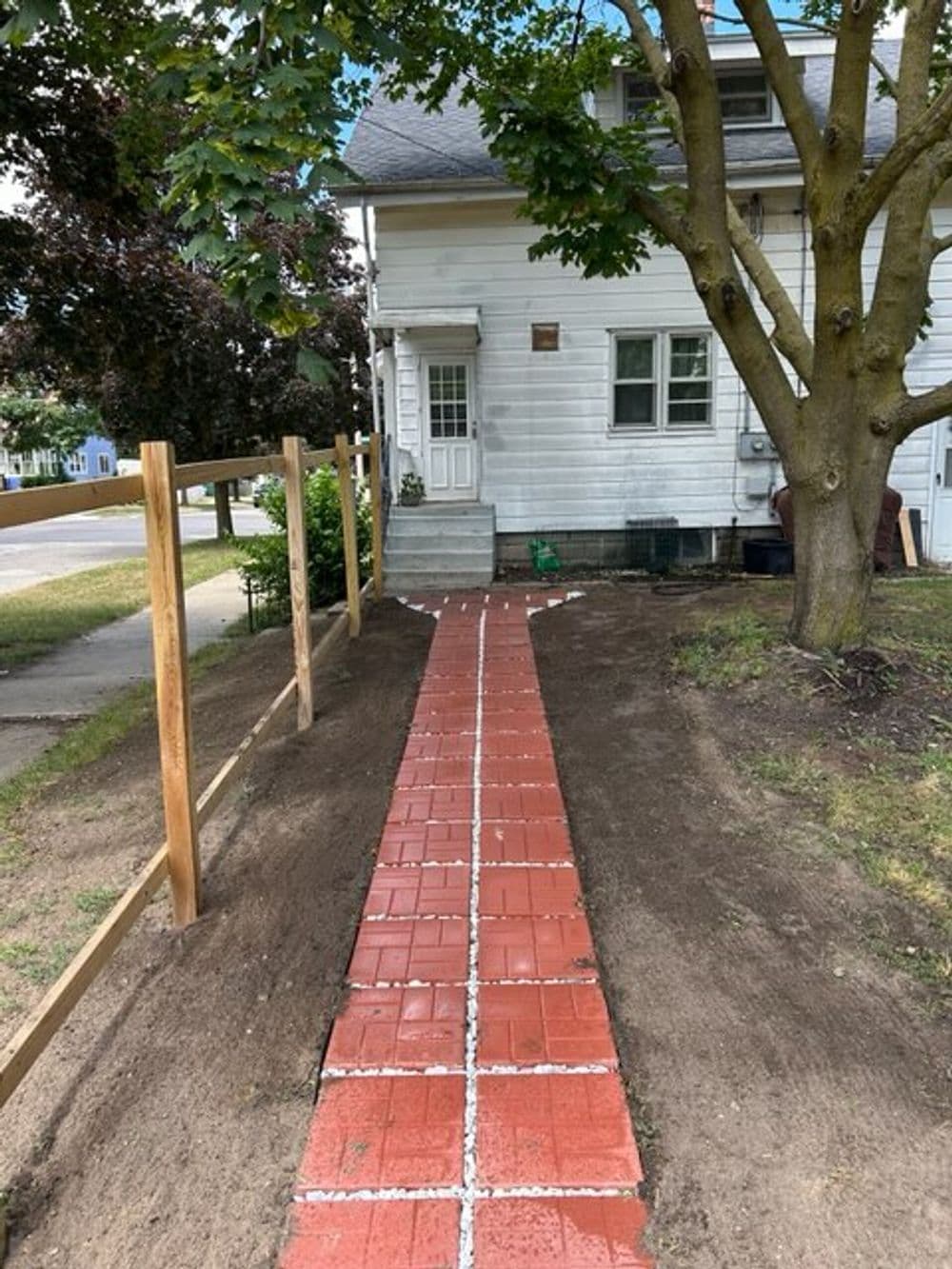 Newly laid red brick walkway lined with gravel leading to a house entrance, surrounded by trees.