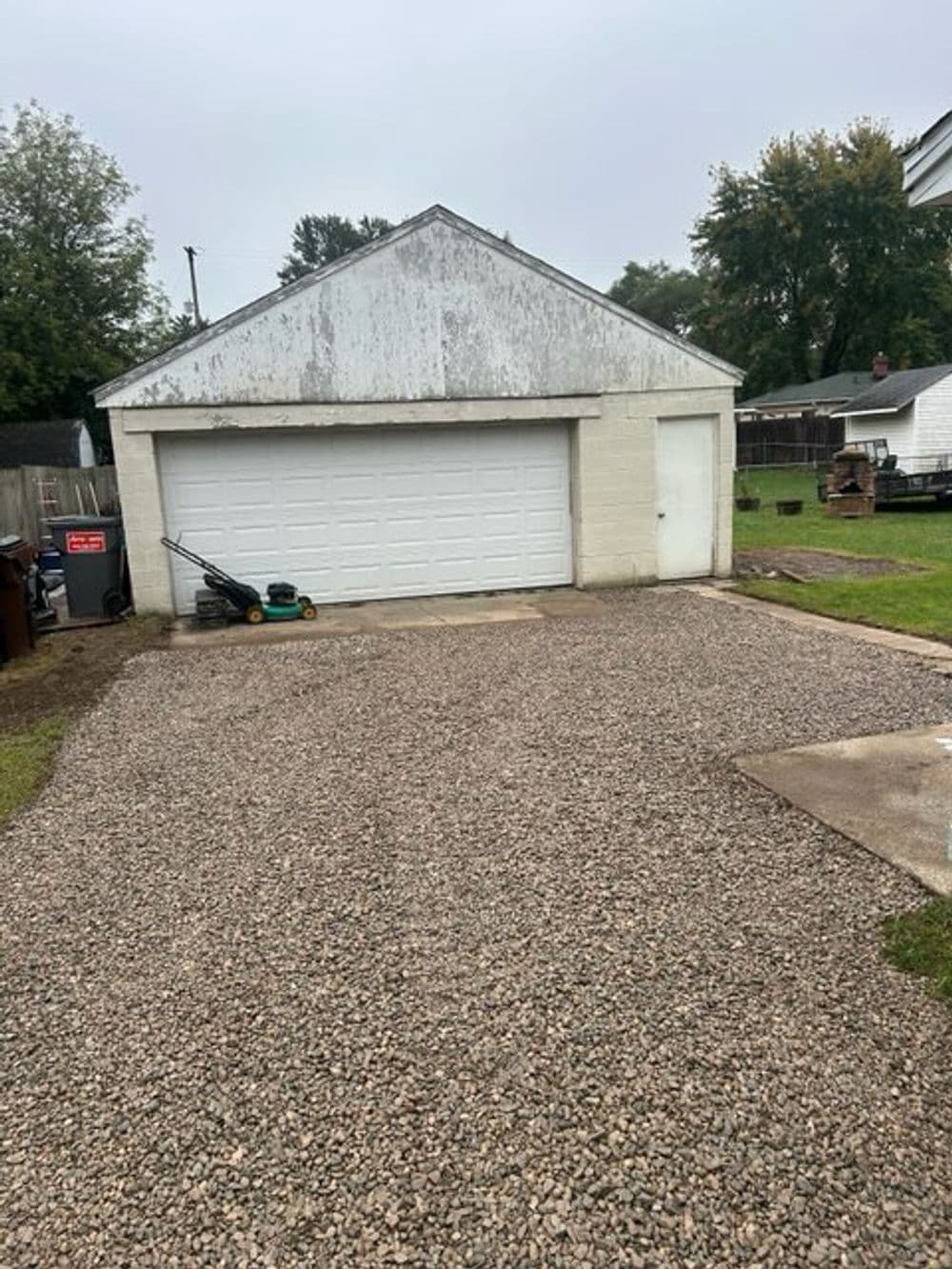 Two-car garage with white siding, surrounded by gravel and lawn equipment in a residential area.