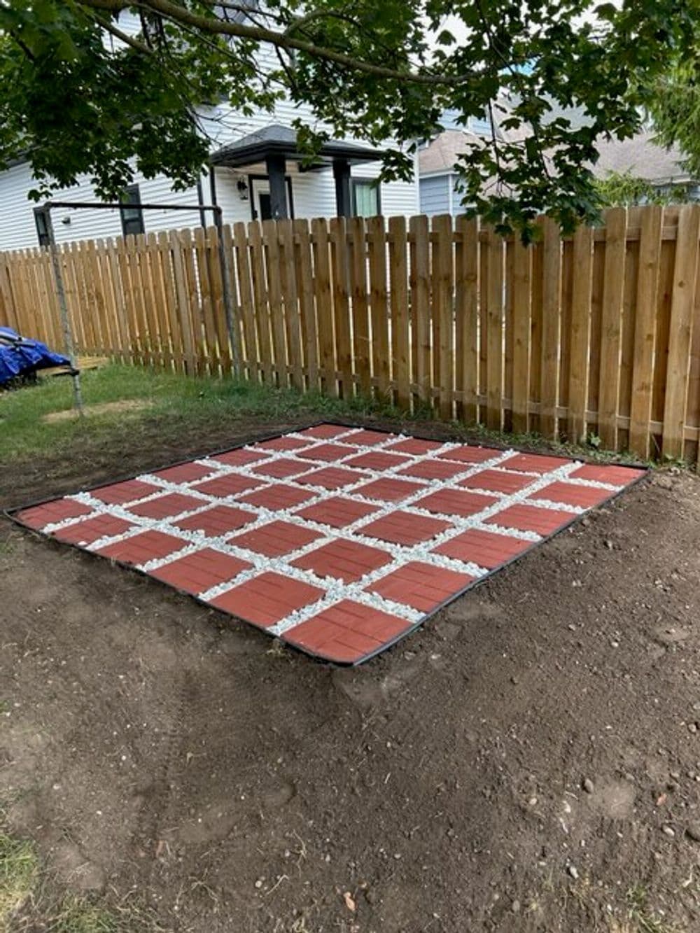 Garden patio area with red paving stones and white gravel, surrounded by wooden fence.