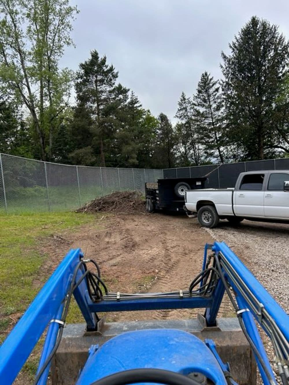 View from a tractor's dashboard showing a trailer and pickup truck in a wooded area.
